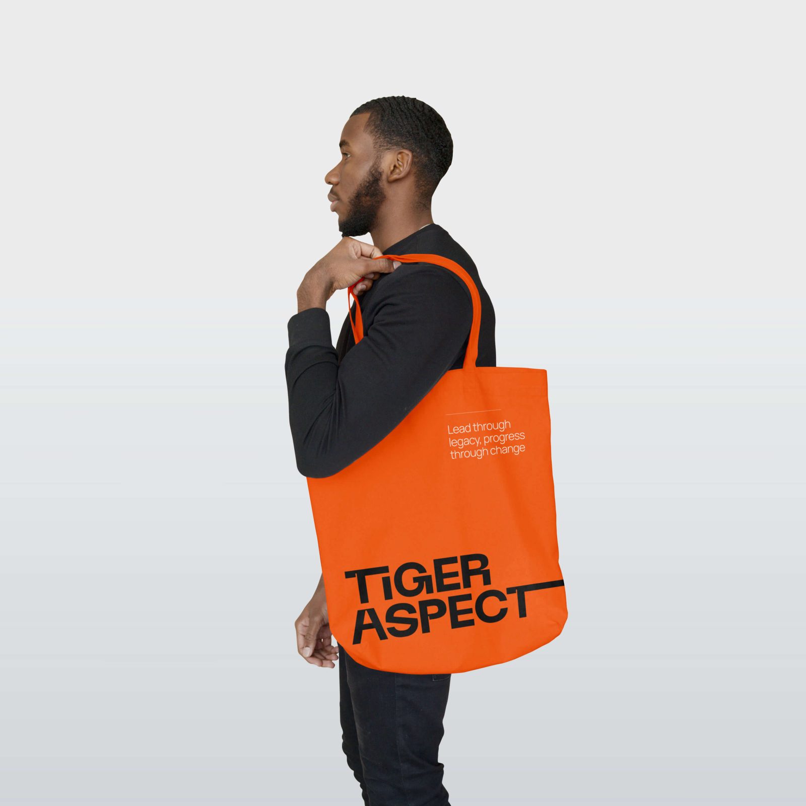 A man in profile, wearing a black top and carrying a bright orange tote bag with the text 