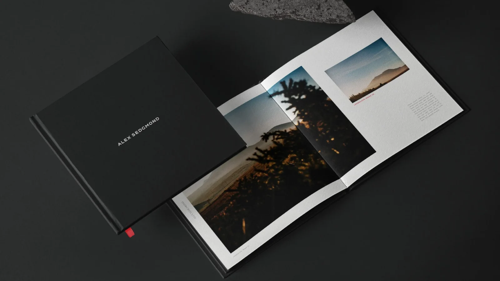 A hardcover photo book open on a dark surface displaying landscape photographs; the left page shows a sunny coastal scene and the right page includes a mountain vista designed by a design agency in Bristol.