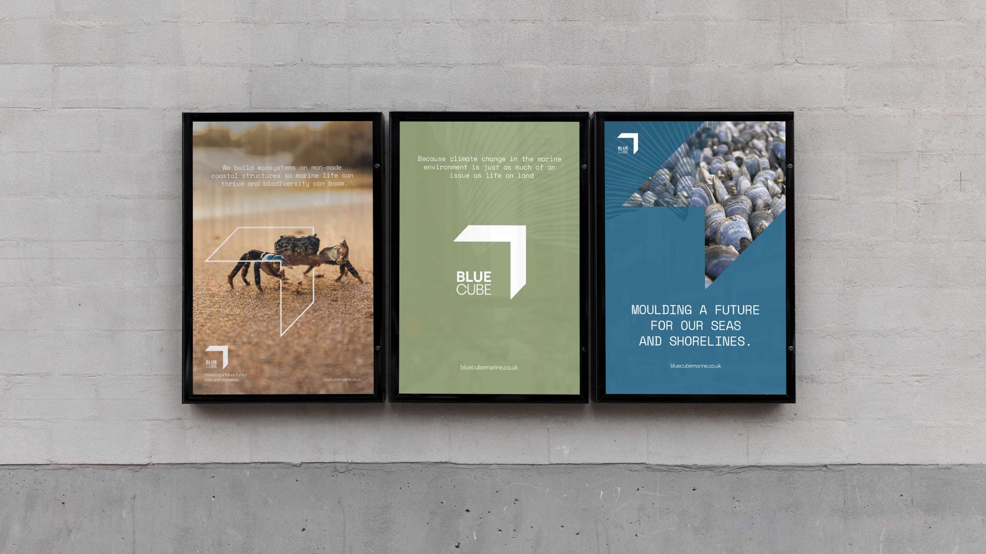 Three framed posters mounted on a concrete wall, each promoting environmental sustainability with images of a robotic device on arid land, a geometric blue cube, and hands holding earth designed by a Brand Agency UK.