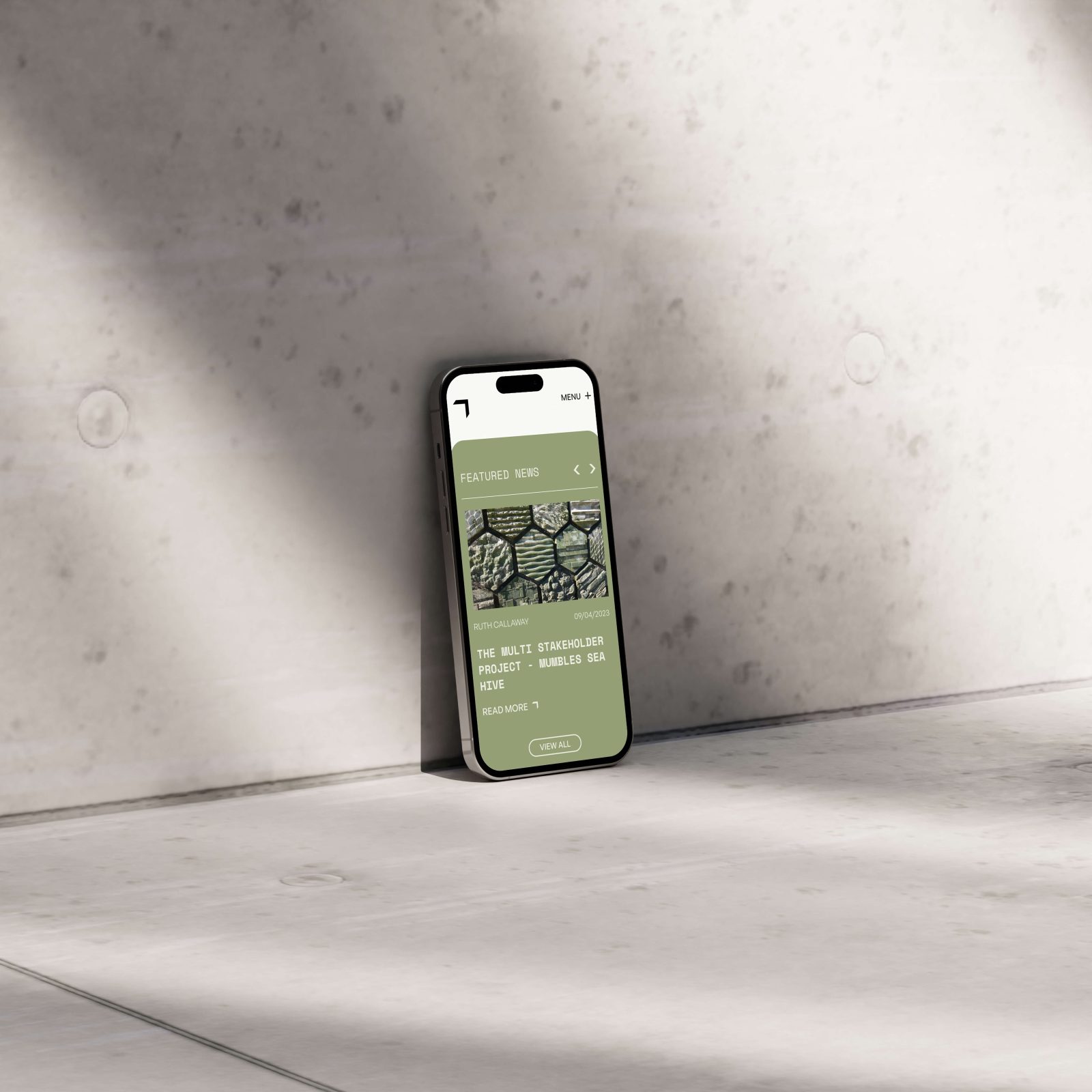 A smartphone displaying a website design by a web agency in Bristol, featuring sunglasses stands upright against a textured light grey wall in a bright environment.