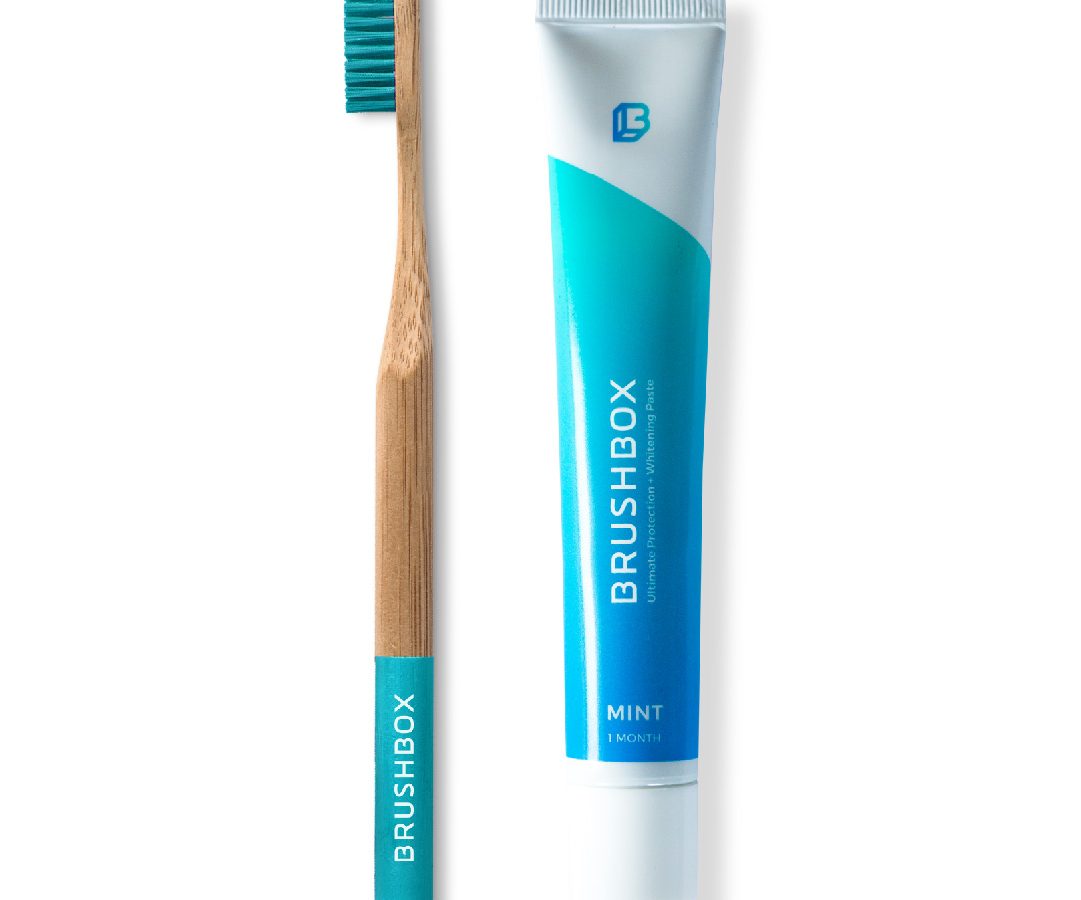 A bamboo toothbrush next to a tube of mint toothpaste labeled 