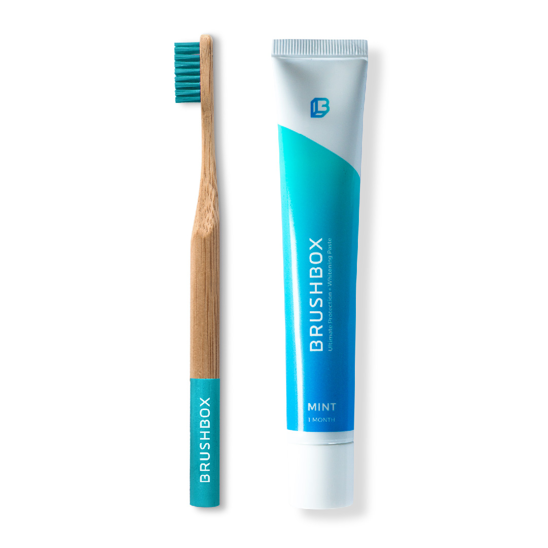 A bamboo toothbrush next to a tube of mint toothpaste labeled 