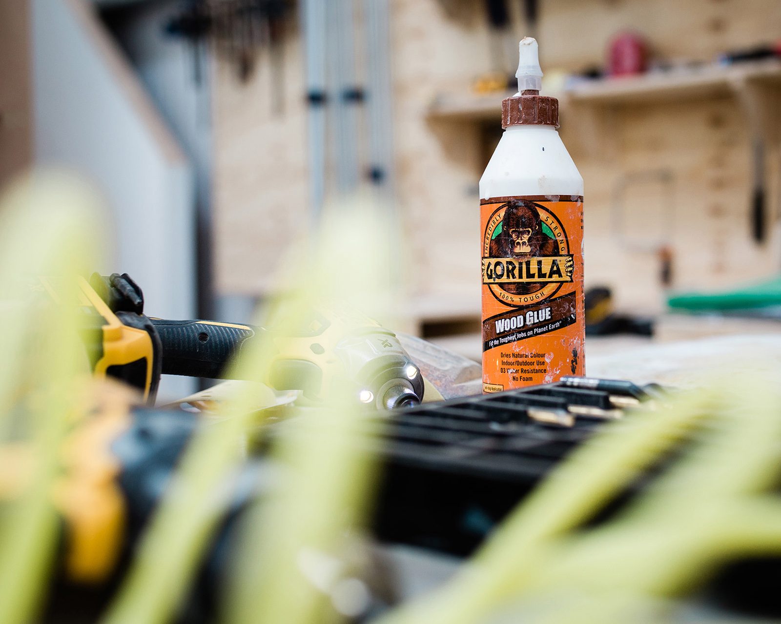 A bottle of gorilla wood glue on a workbench with blurred tools and wood pieces in the background in a woodworking workshop, captured for the portfolio of a Design Agency Bristol.