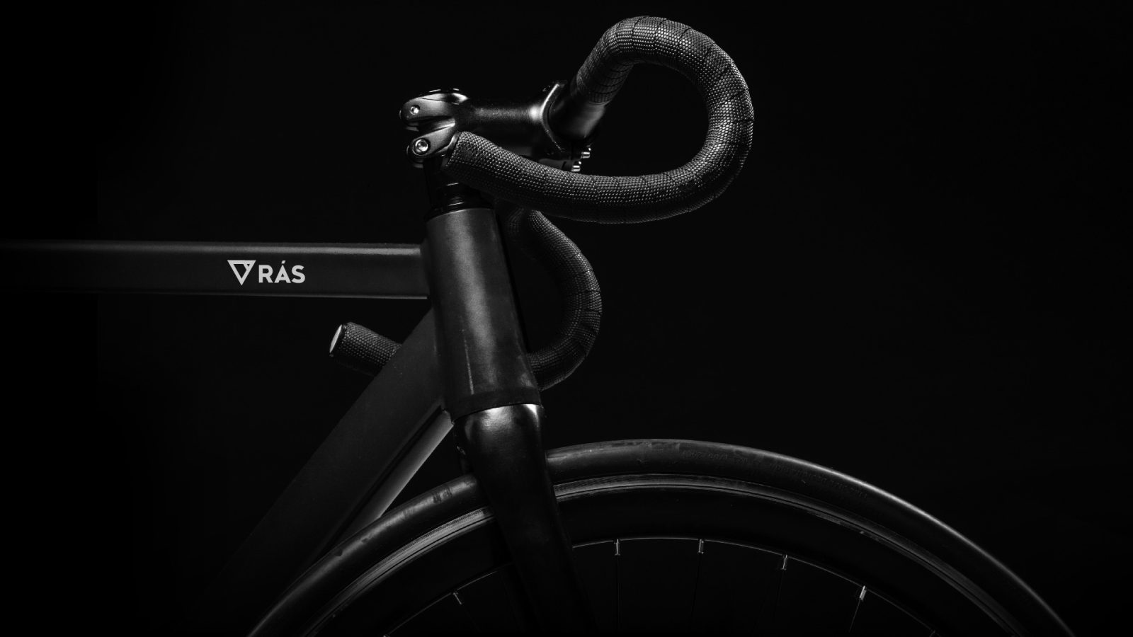 Close-up of a black racing bicycle handlebar and front frame against a dark background, highlighting its sleek brand design and minimalistic aesthetics.