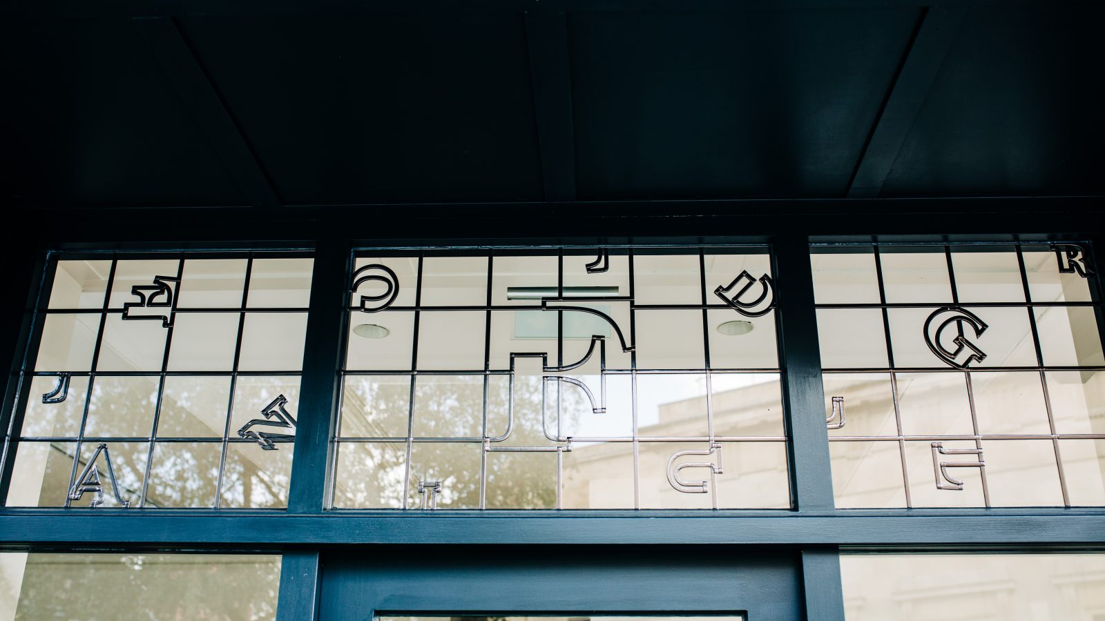 A row of square glass window panes set in a blue frame, each featuring a different black and white geometric shape that incorporates various letters, designed by a brand design agency. The view through the windows