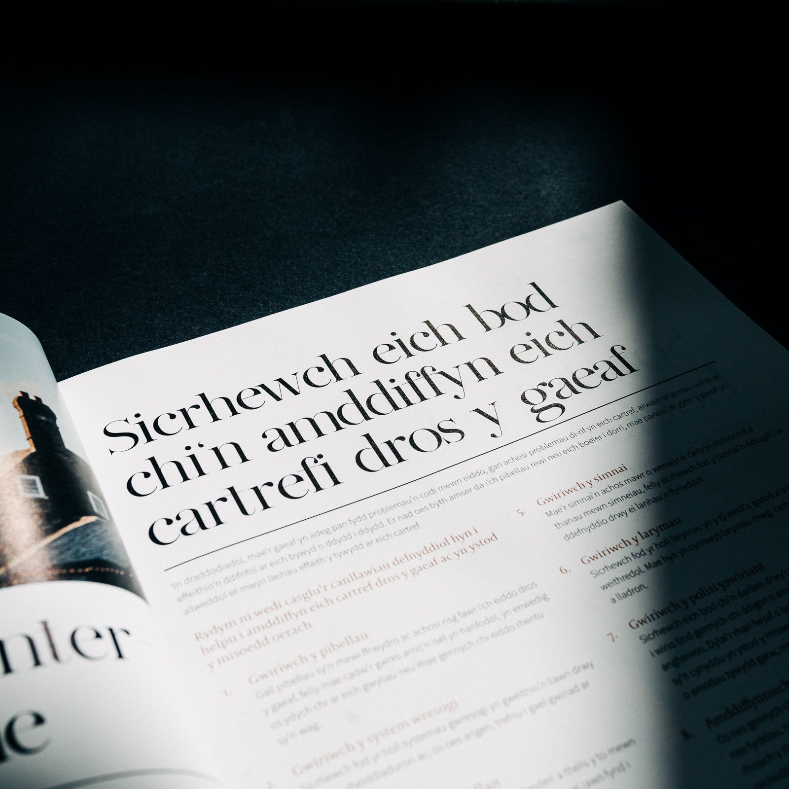 Open magazine featuring an article with text in multiple languages, dramatically lit under a beam of light on a dark background, courtesy of Design Agency Bristol.