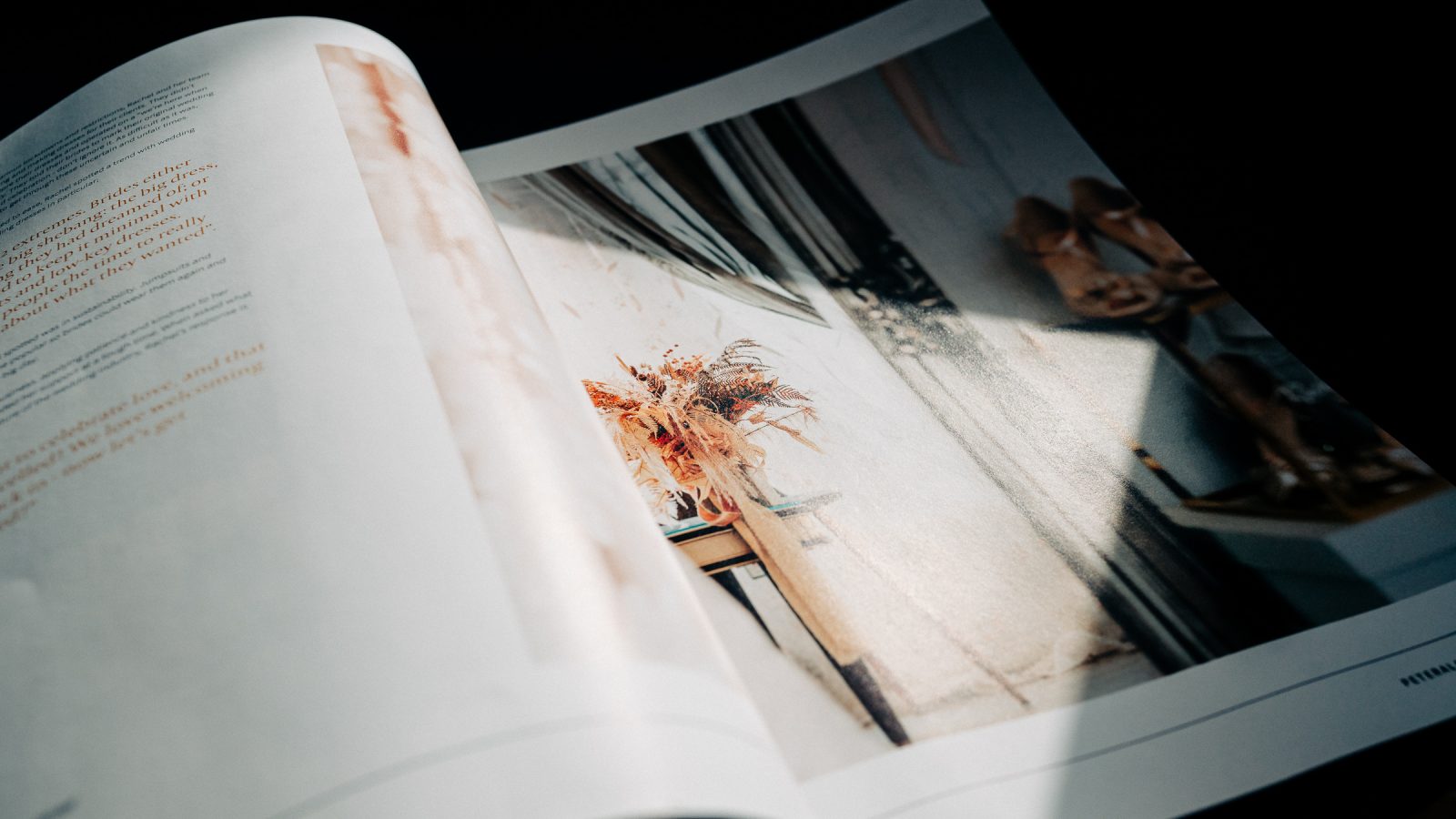 An open magazine with a close-up photo of an article page featuring a brightly lit image of a flower vase on a table, designed by Design Agency UK, with soft shadows and text on the left side