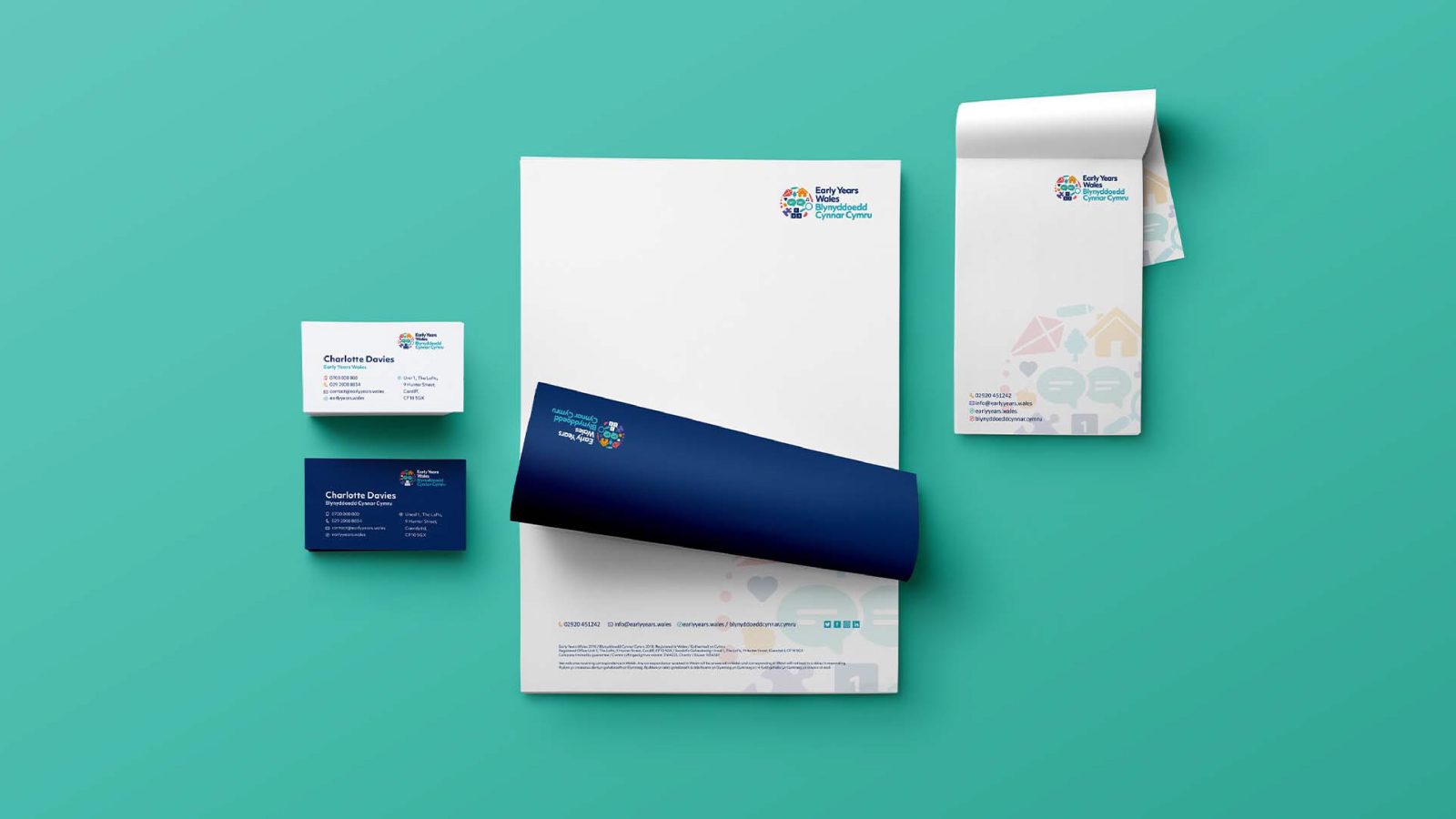 Corporate branding materials designed by a prominent Design Agency UK, including a business card, letterhead, and envelope displayed on a teal background, all featuring a logo with colorful iconography.