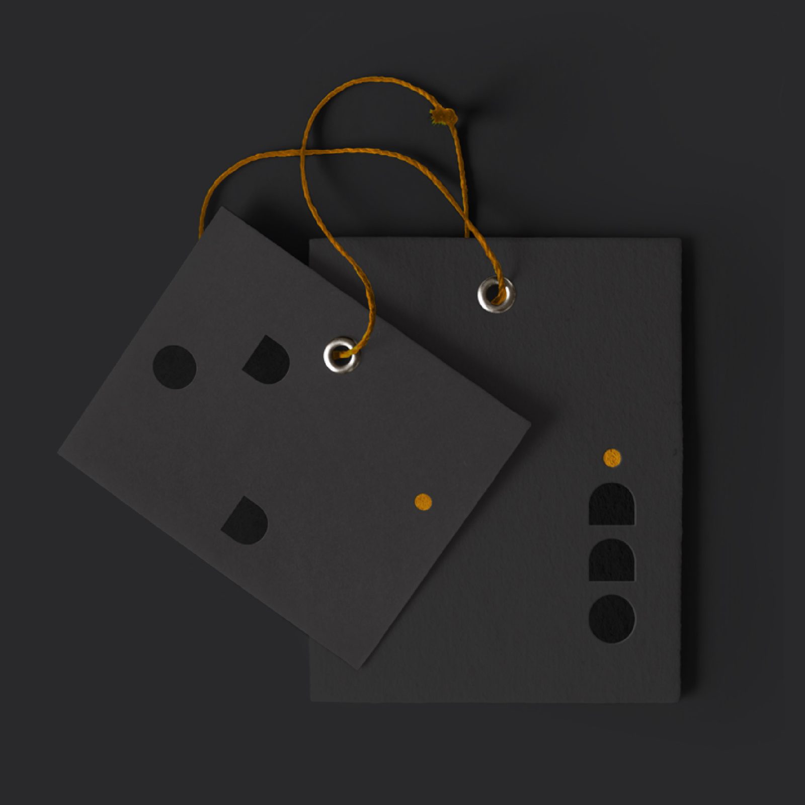 Two black tags with a brand design featuring geometric shapes, connected by a yellow string, displayed against a dark background.
