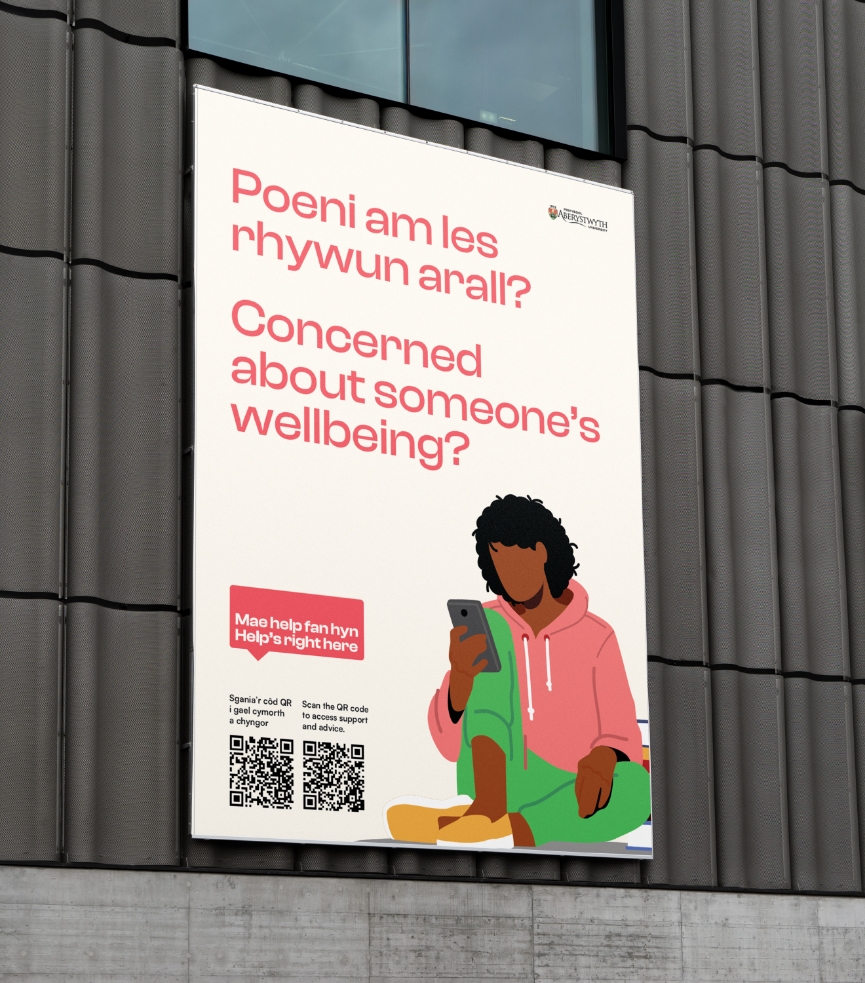 A billboard on a building featuring an illustration of a person sitting and reading a message on a phone. The text, inquiring about well-being concerns in Welsh and English, includes a QR code, hotline