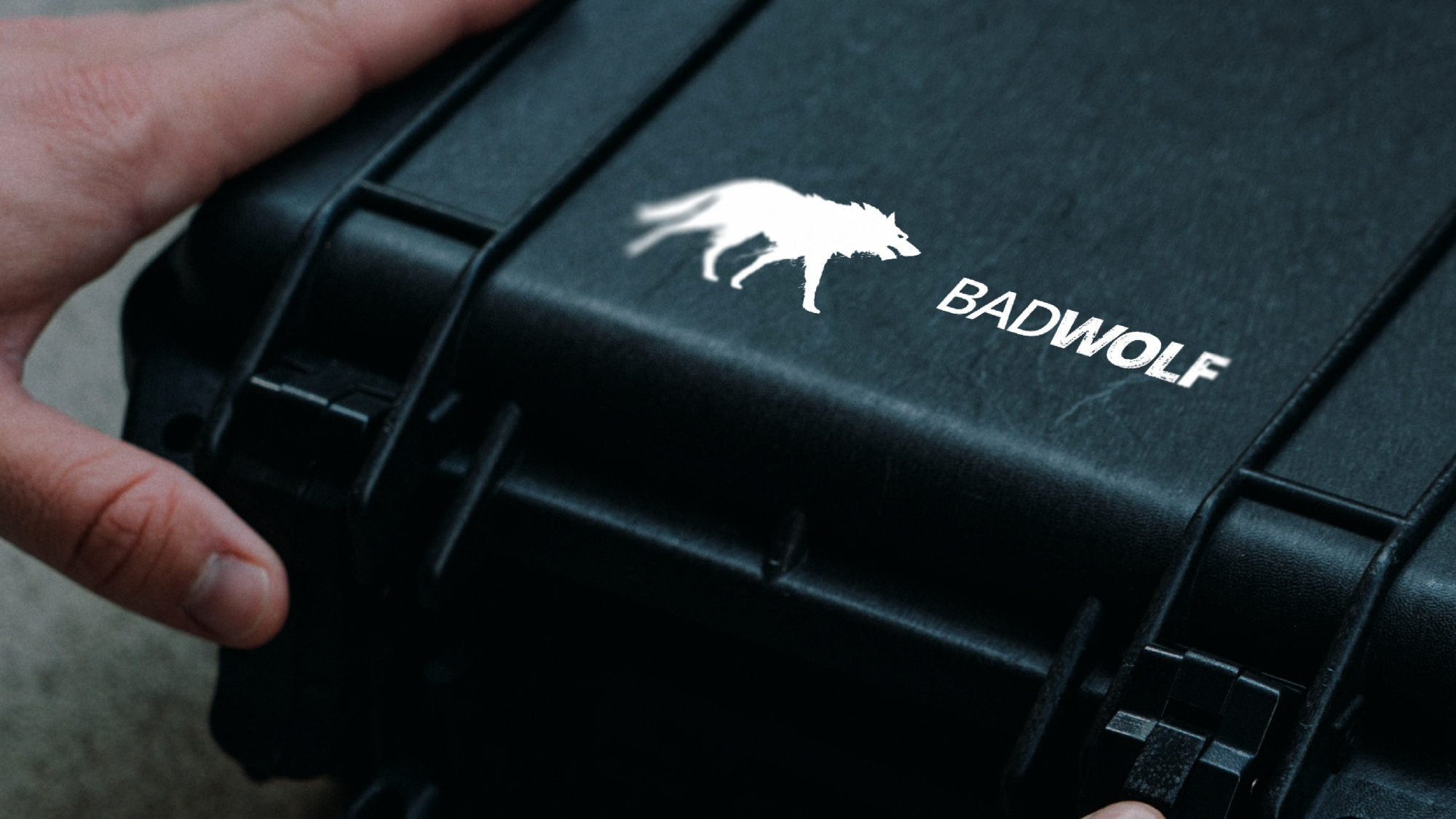 A person holds a closed black protective case with a white logo of a wolf and the word 