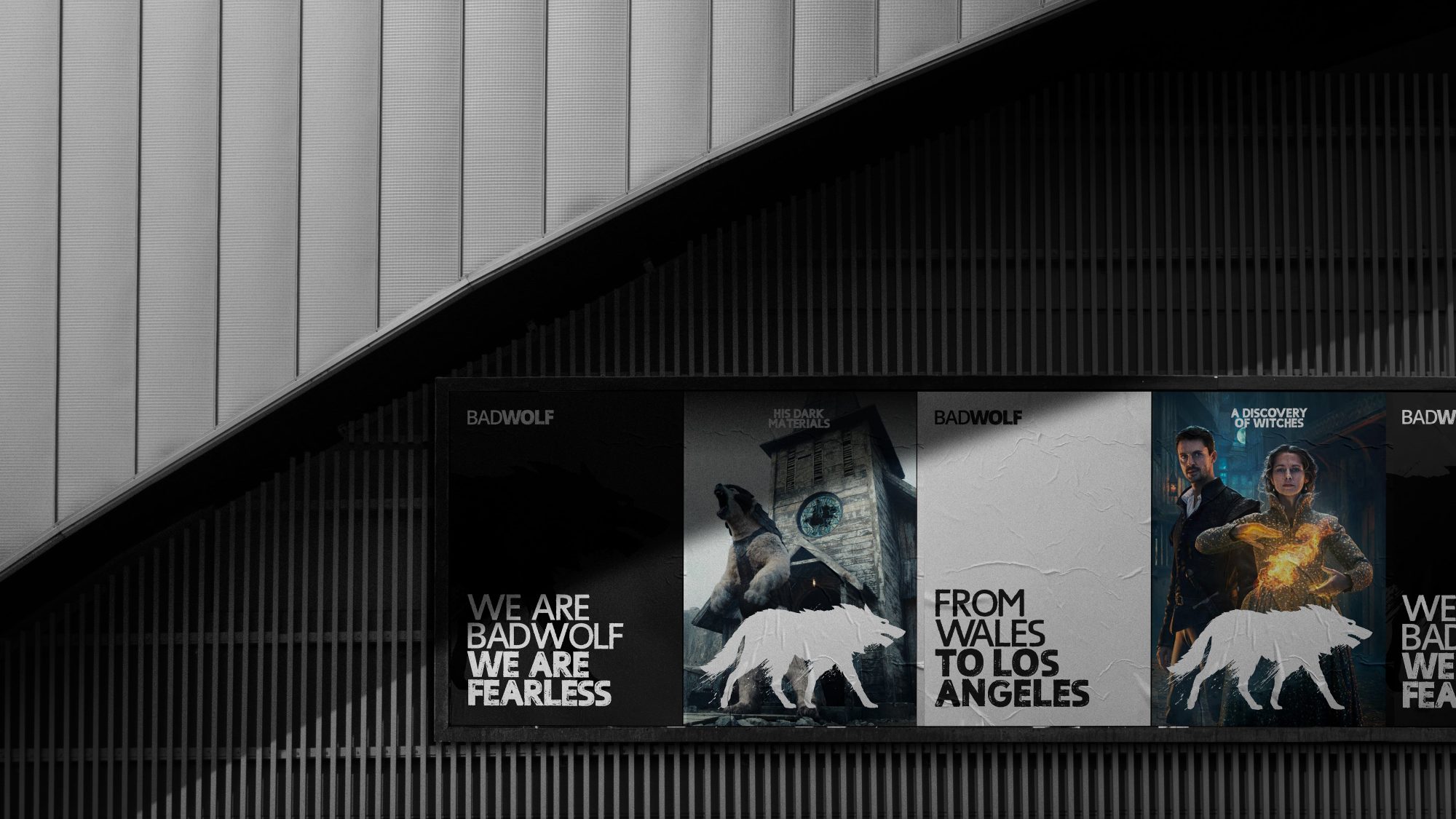 A diagonally angled view of a dark modern building facade with three illuminated posters advertising a web design agency named 