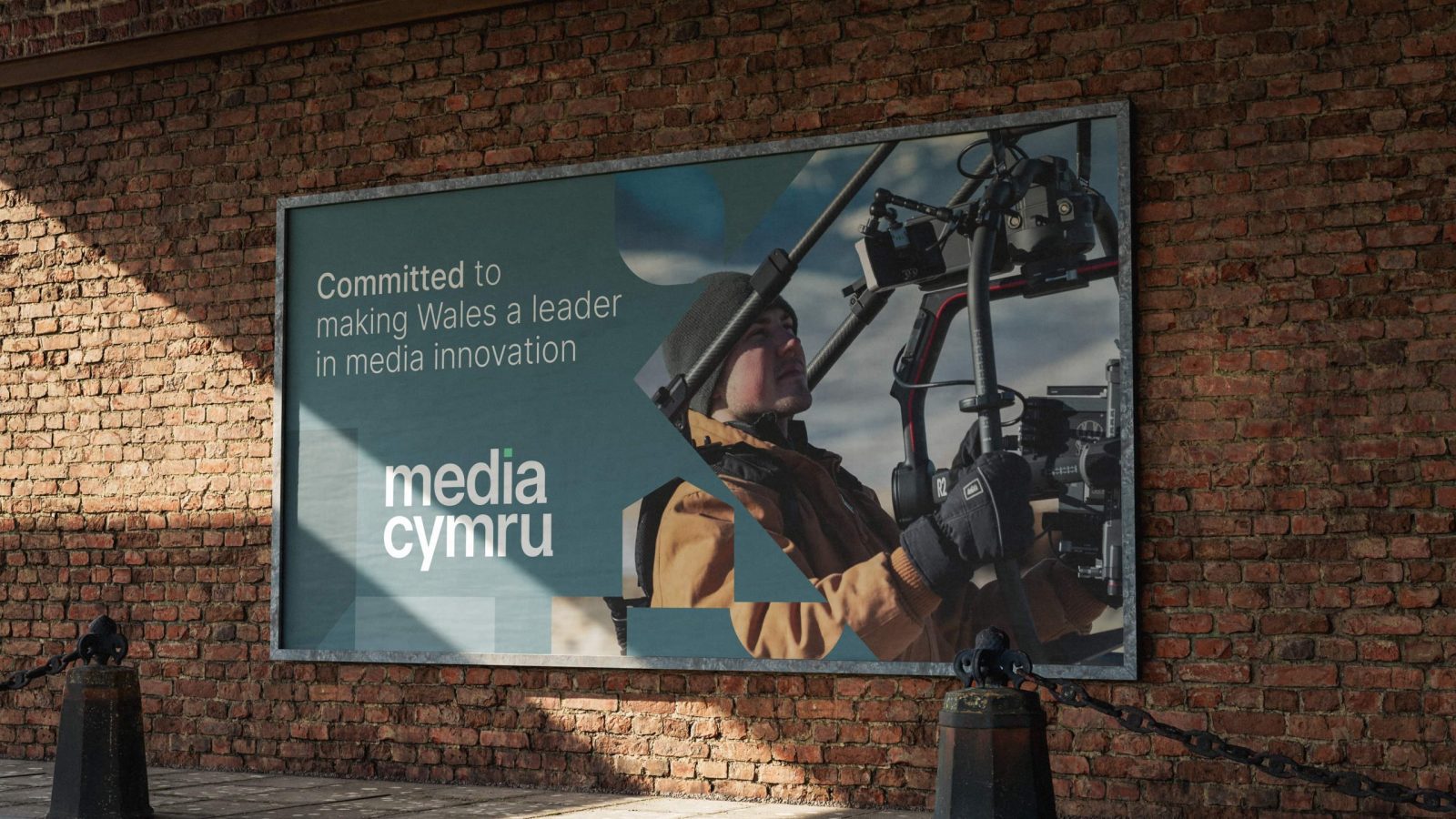 A billboard on a brick wall displays a person operating a camera, accompanied by the text 