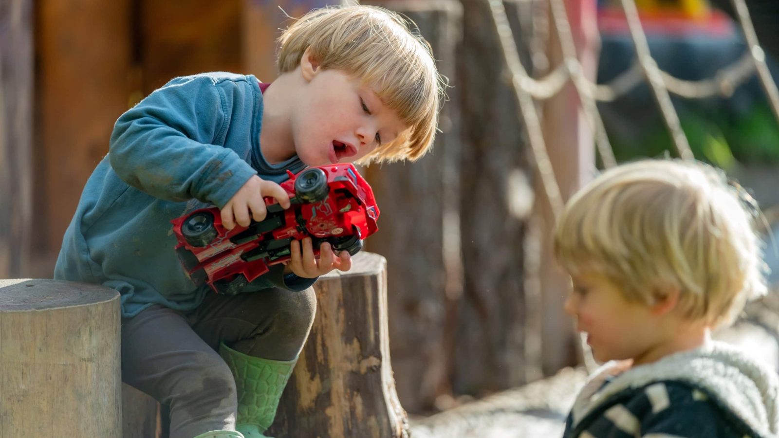 A young boy in a blue shirt, intensely focused on fixing a red toy car, as another boy watches him, seated outdoors on a sunny day. This scene was captured for a brand strategy campaign demonstrating