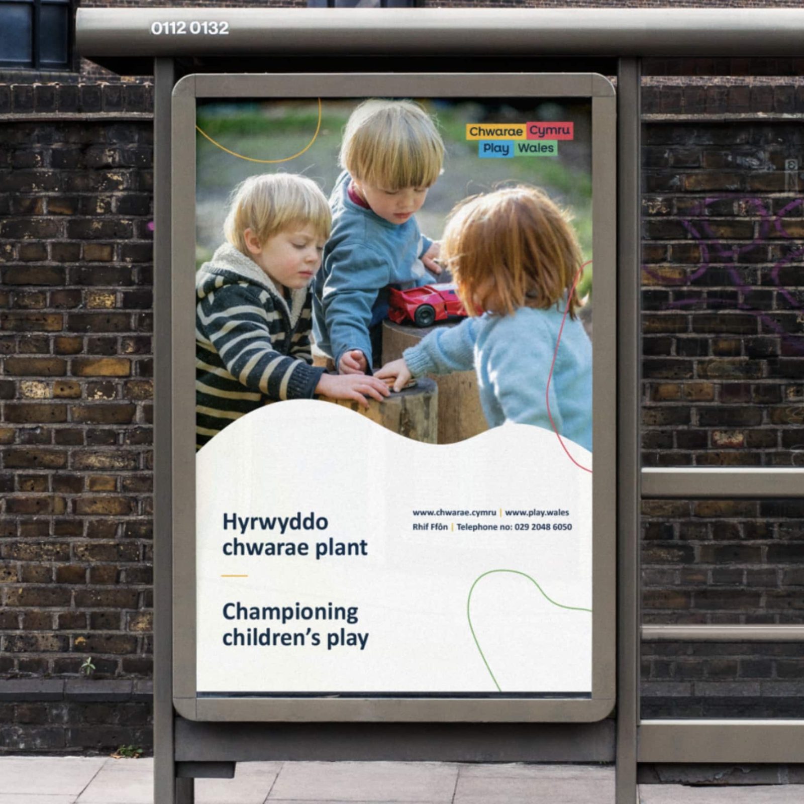 An outdoor advertisement, designed by a prominent Brand Agency in Cardiff, features an image of three young children playing with a red toy car on a low wall. This display promotes children's play with bilingual text