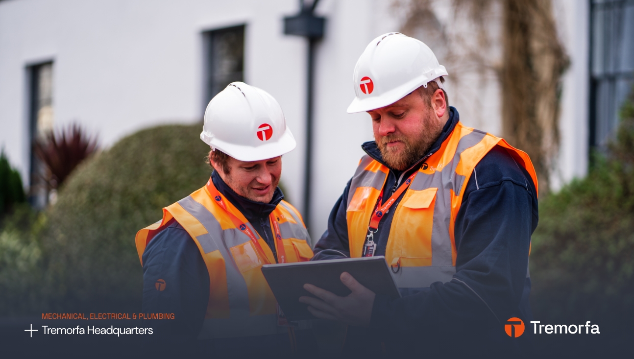 Two construction workers in high-visibility vests and white helmets discuss graphic design plans on a tablet outside the Tremorfa headquarters.