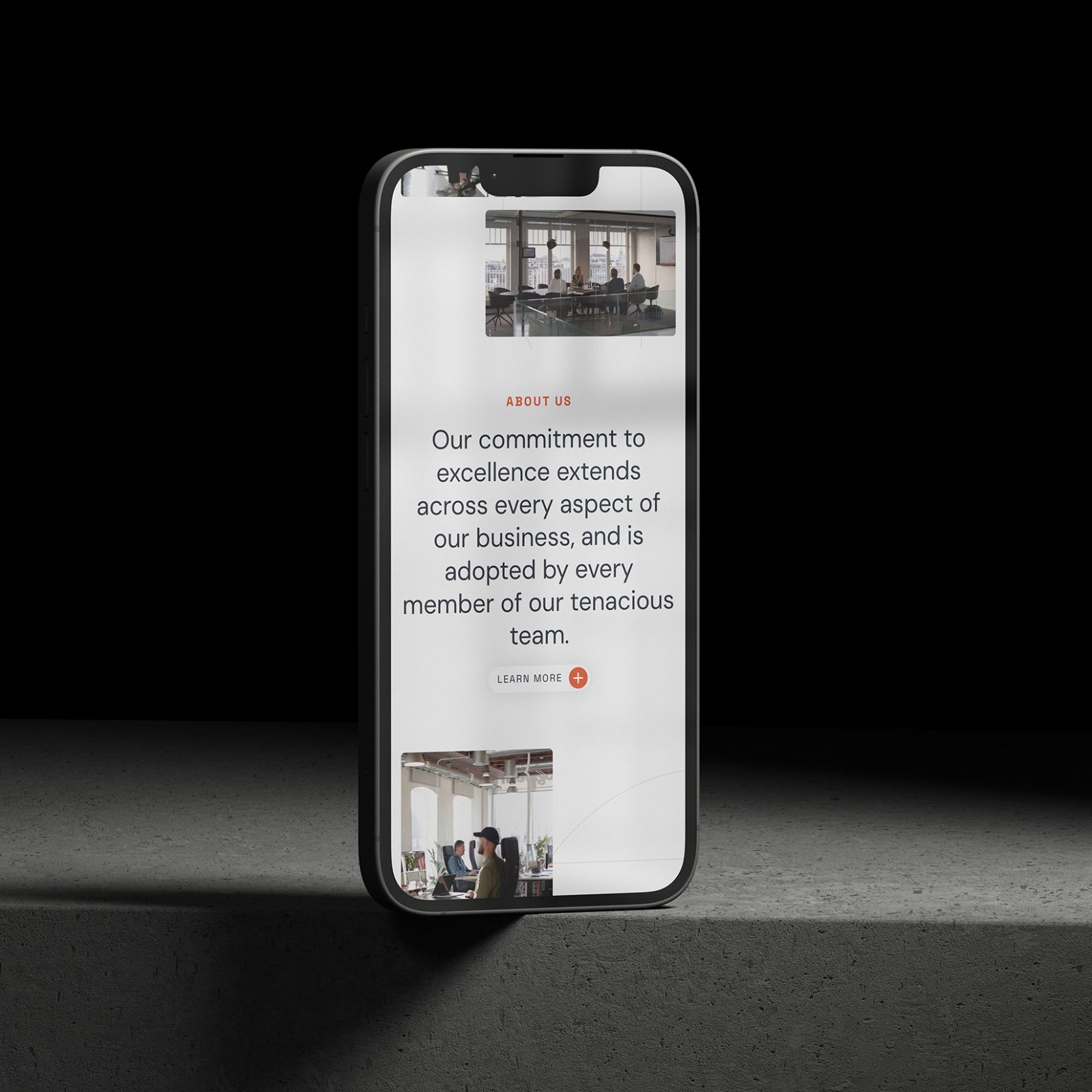 A smartphone displaying a company website with text about commitment to excellence and a team photo on a concrete surface. The phone, highlighted by a spotlight, features the work of Design Agency Wales on its screen.