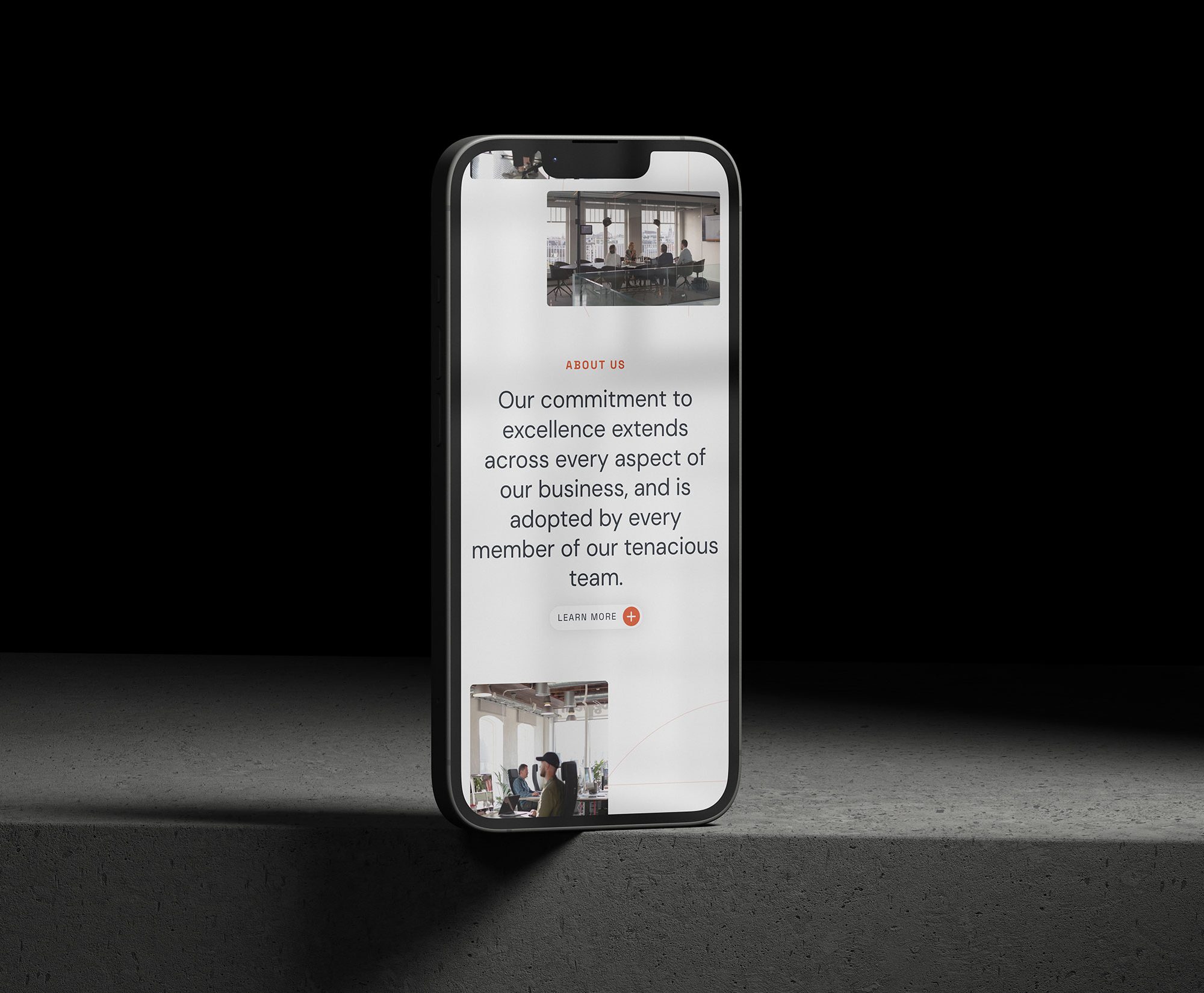 A smartphone displaying a company website with text about commitment to excellence and a team photo on a concrete surface. The phone, highlighted by a spotlight, features the work of Design Agency Wales on its screen.