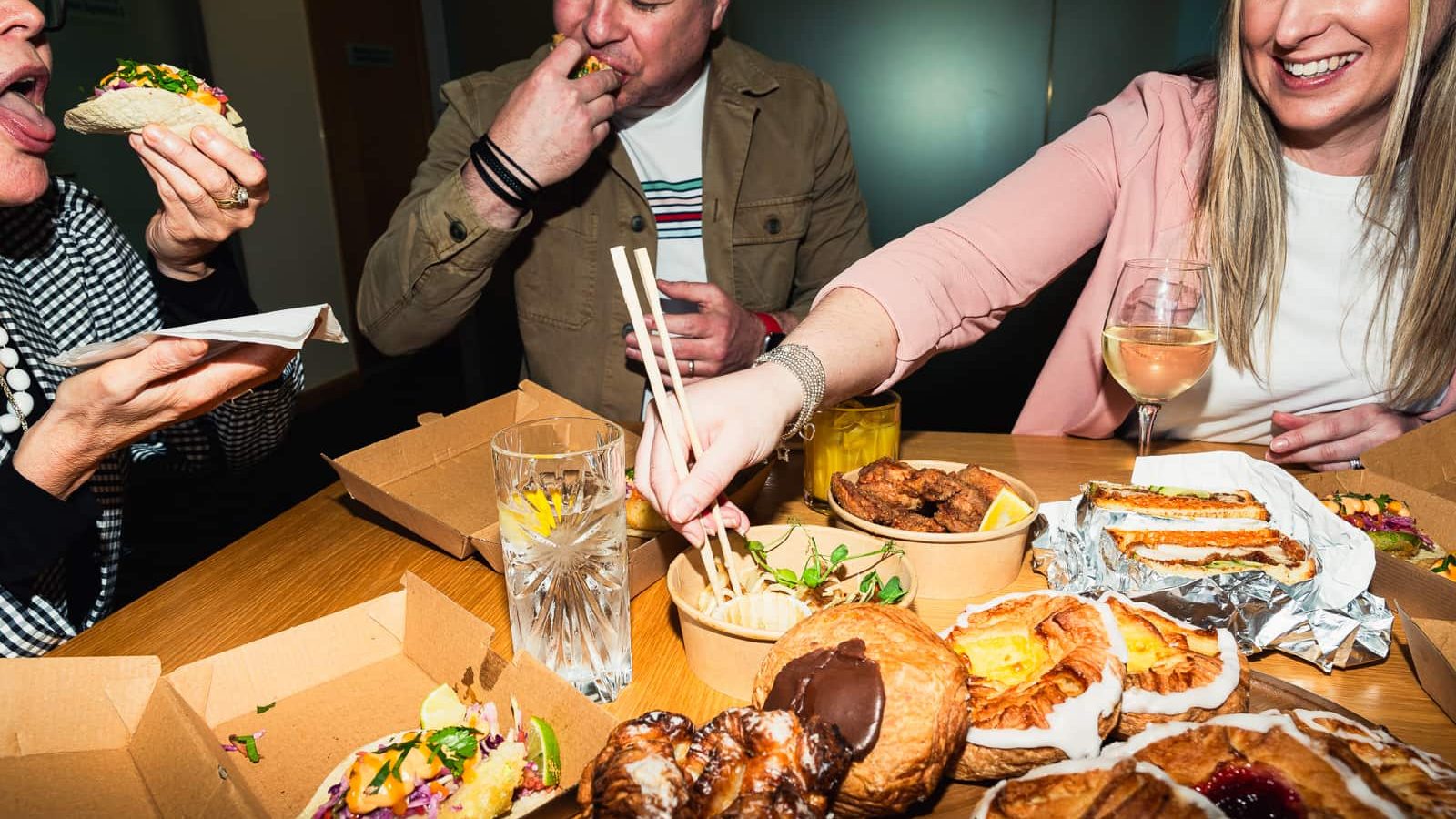 People savoring a meal with diverse foods, including pastries and various dishes, gather at a table with drinks and wine. The scene feels timeless and inviting, as if the bad wolf himself might linger nearby, drawn in by the irresistible aromas.