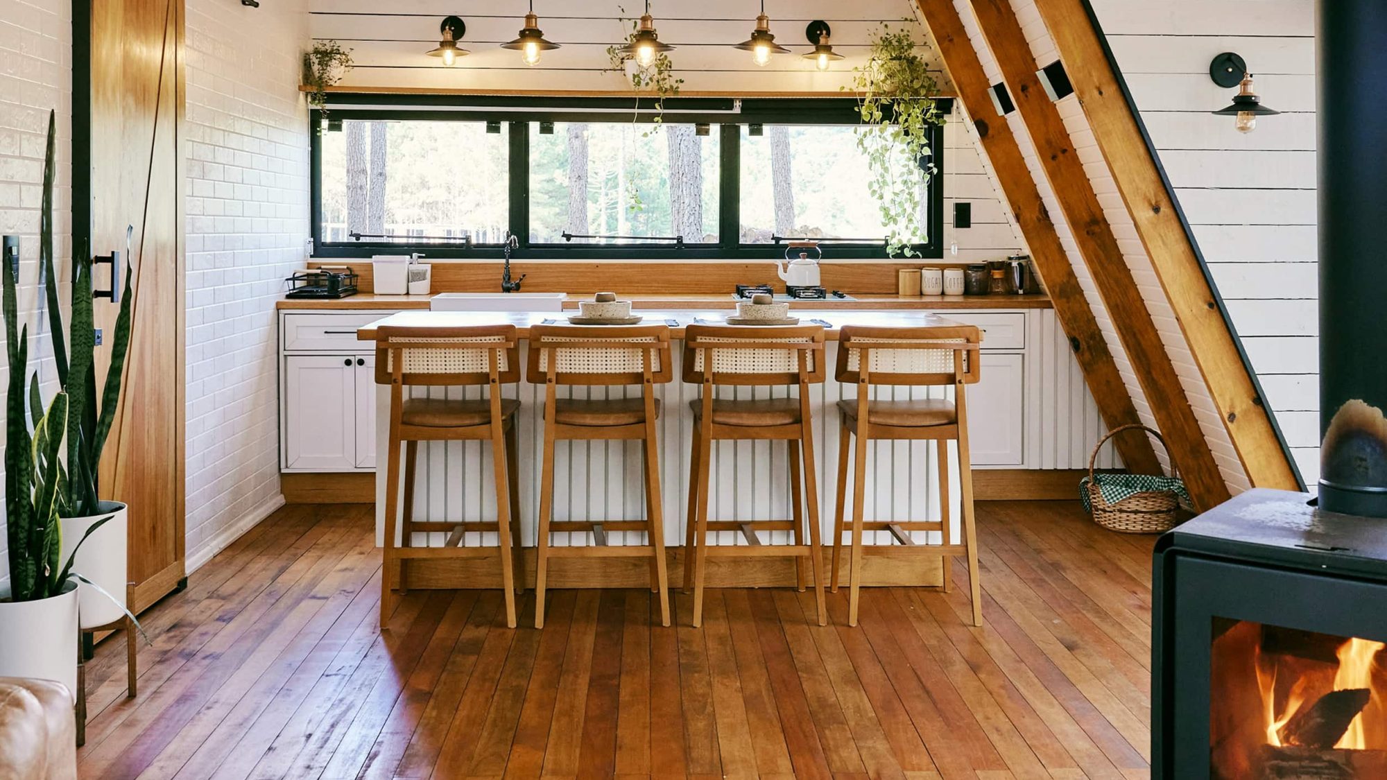 A modern kitchen with white cabinets, wooden island and flooring, hanging lights, and a wood-burning stove - beware the bad wolf.