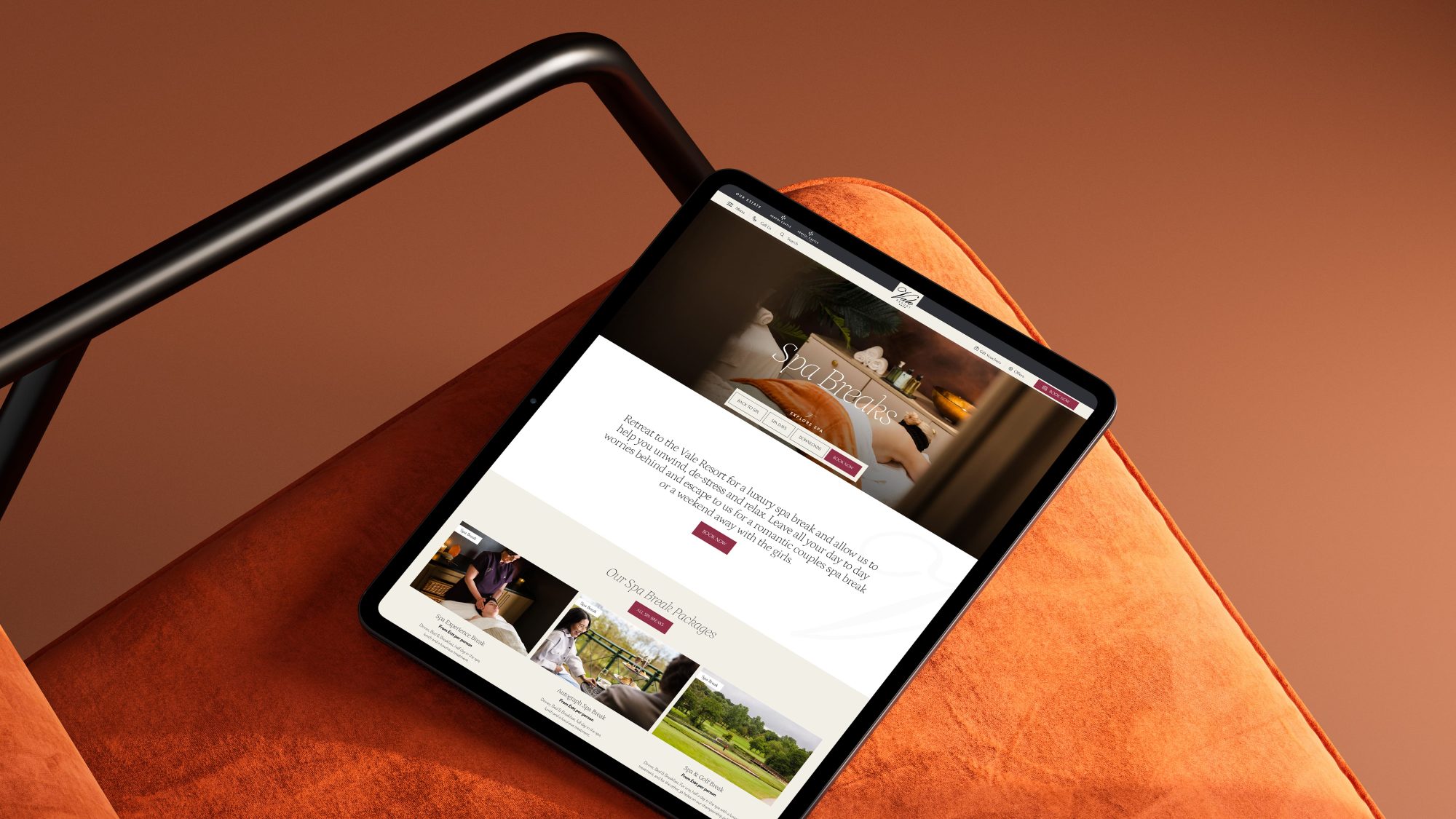 A tablet displaying The Vale Resort website rests on an orange chair, with a staircase railing in the background.