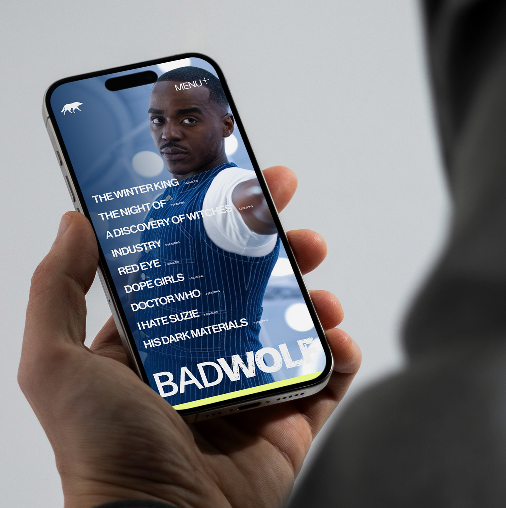 Designdough-Badwolf-mobile-showreel-design Person holding a phone showing a streaming app with a man’s face and TV show titles like
